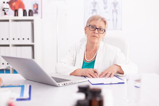 Mature female doctor wearing lab coat in hospital room while using laptop. Medical practitioner using notebook in clinic workplace , confident, expertise, medicine.