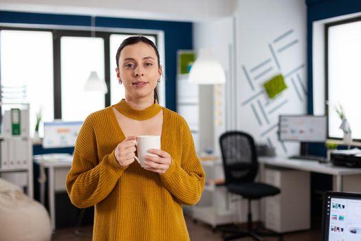 Portrait of business woman holding cup of coffee in start up companny office smiling looking at camera. Executive entrepreneur, manager leader standing working on projects.