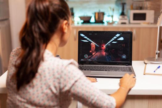 Lady playing games on laptop during night time during night time in home kitchen. Professional gamer playing online videop games on her personal computer. Geek cyber e-sport.