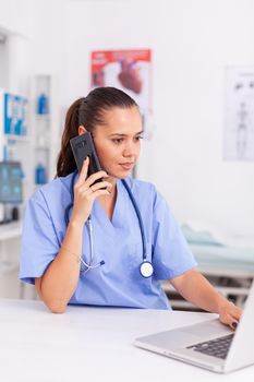 Medical receptionist talking with patient in hospital office and using laptop . Health care physician sitting at desk using computer in modern clinic looking at monitor.