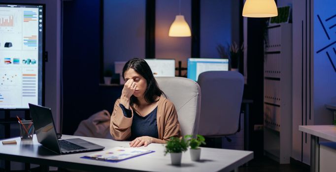 Portrait of of stressed at work doing overtime to complete important task. Employee falling asleep while working late at night alone in the office for important company project.