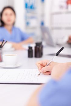 Medical nurse writing on clipboard during healthcare seminar in hospital meeting office about technology. Clinic expert therapist talking with colleagues about disease, medicine professional.