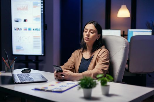 Caucasian entrepreneur messaging in the course of working in the evening. Businesswoman texting late at night while working on important project using smartphone .