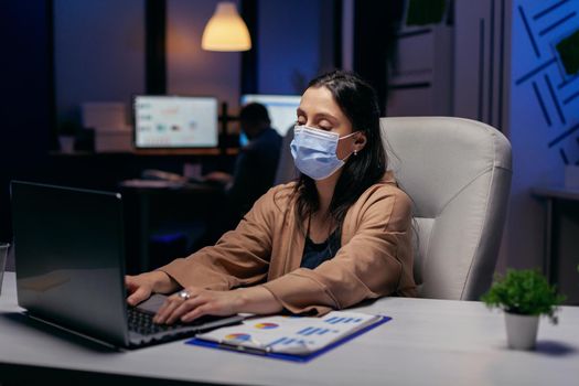 Businesswoman working hard to finish a deadline due to covid19 outbreak. Woman following social distancing rules due to coroanvirus pandemic while working late hours at the office.