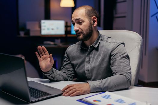 Entrepreneur greeting people during online call to talk about future project. Businessman in the course of an important video conference while doing overtime at the office.