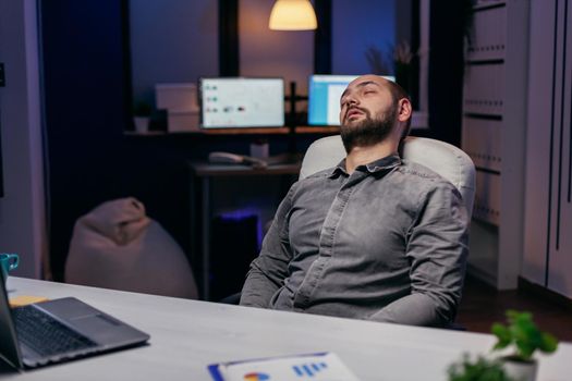 Young businessman resting on chair while working on deadline. Workaholic employee falling asleep because of while working late at night alone in the office for important company project.