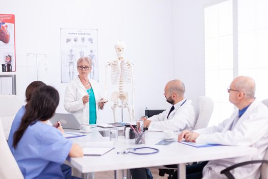 Medical scientist doing demonstration with human skeleton in conference room with her team. Clinic expert therapist talking with colleagues about disease, medicine professional