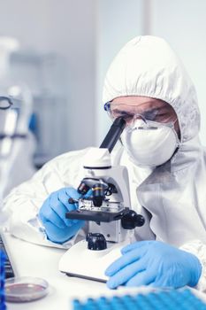 Medical engineer adjusting microscope while doing coronavirus investigation Scientist in protective suit sitting at workplace using modern medical technology during global epidemic.