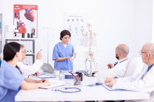 Female nurse working with human skeleton during presentation in front of doctors for examination. Clinic expert therapist talking with colleagues about disease, medicine professional