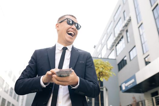 Successful business man counting money. Smiling man enjoy good deal near modern office. Man made easy money. Rich man in stylish suit wearing sunglasses counting money