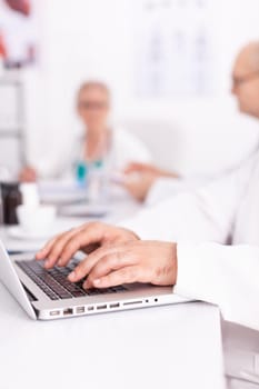 Close up of doctor hands typing on laptop keyboard during meeting with his medical team. Clinic expert therapist talking with colleagues about disease, medicine professional