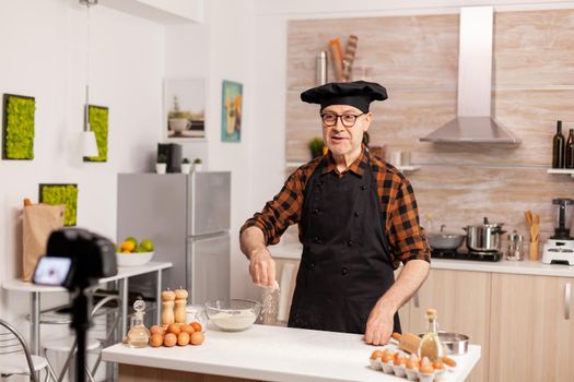 Baker presenting how to use wheat flour while recording video tutorial. Retired blogger baker influencer using internet technology communicating, shooting, blogging on social media with digital equipment