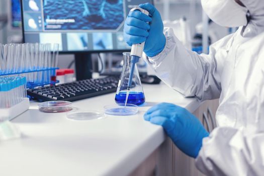 Doctor working to find a cure for coronavirus using micropipette and petri dish wearing protective suit and face mask. Chemist in modern laboratory doing research using dispenser during global epidemic with covid-19.