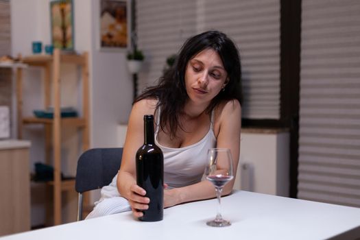 Unhappy woman with alcohol addiction drinking wine alone feeling depressed and intoxicated. Young adult with bottle of wine and glass using liquor for sadness, loneliness and desperation