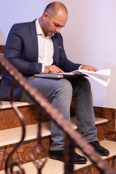 Overworked tired businessman working to finish financial project before deadline doing overtime. Entrepreneur working late in evening corporate sitting on stairs in building office.