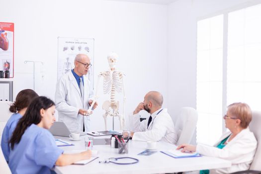 Team of scientist examining and study human skeleton in meeting room to come up with diagnosis. Clinic expert therapist talking with colleagues about disease, medicine professional.