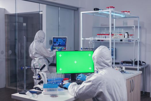 Computer with green screen in lab and medical staff dressed in ppe suit during coroanvirus. Team of microbiologists doing vaccine research writing on device with chroma key, isolated, mockup display.