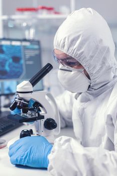 Close up of chief researcher scientist adjusts microscope in time of coronavirus experiment. Virolog in coverall during coronavirus outbreak conducting healthcare scientific analysis.
