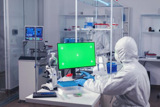 Engineer in laborator during coronavirus pandemic working on computer with green screen. Team of microbiologists doing vaccine research writing on device with chroma key, isolated, mockup display.