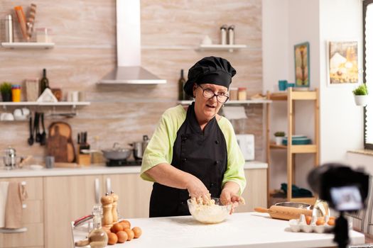 Senior woman recording live video for culinary vlog at home. Retired blogger chef influencer using internet technology communicating, shooting blogging on social media with digital equipment