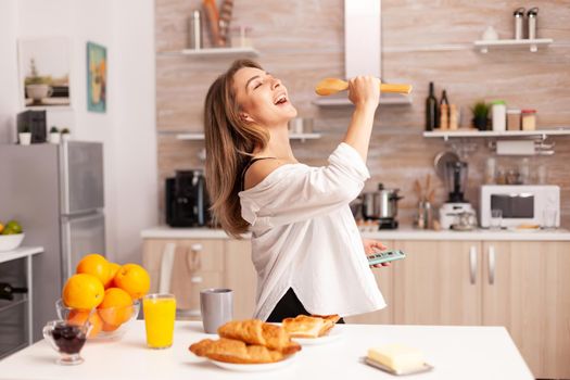 Woman singing during breakfast in home kitchen wearing sexy lingerie. Seductive woman with tattoos using smartphone wearing temping underwear in the morning.