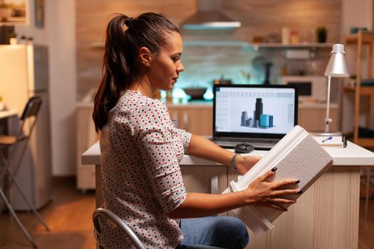 Serious architect working on a housing project holding a building model during late night time. Engineer artist creating and working in office holding scale building model, determination, career.