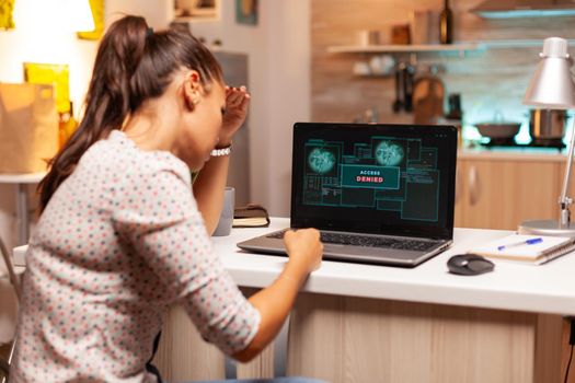 Angry hacker woman because of access denied while trying to attack government firewall. Programmer writing a dangerous malware for cyber attacks using performance laptop during midnight.