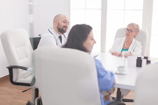 Medical staff smiling in meeting room while talking with other medical practitioner wearing white coat. Clinic therapist with colleagues talking about disease, expert,specialist, communication.