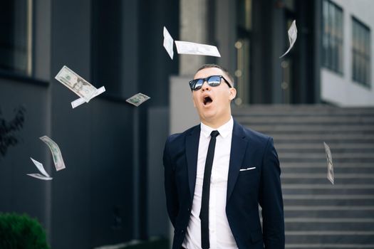 Happy good looking man throwing dollars. Money rain, falling dollars. Portrait shot of cheerful rich handsome businessman in glasses and suit throws money.