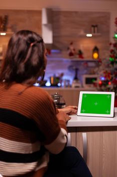 Caucasian adult watching green screen technology on tablet sitting at kitchen counter. Young woman using digital chroma key concept for background template, mockup gadget app on display