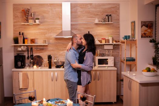 Young couple dancing in kitchen during romantic dinner. Happy in love couple dining together at home, enjoying the meal, smiling, having fun, celebrating their anniversary.