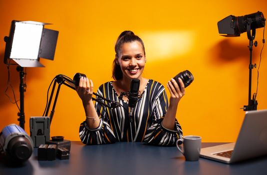 Woman smiling at camera while recording lens review for followers. New media star influencer on social media talking video photo equipment for online internet web show