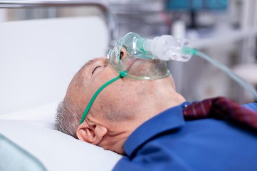 Old male patient weating oxygen mask laying in hospital bed while getting treatment after being infectetd with coronavirus. Medicine medical healthcare system epidemic lungs infection treatment