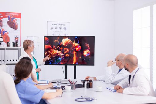 Mature expert doctor talking about global pandemic with coronavirus in conference room for colleagues. Virolog specialist doctor discussing with colleagues about global pandemic because of dangerous virus, symptoms.