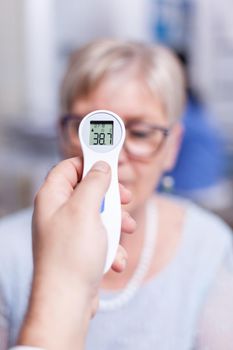 Senior patient having high temperature measured using infrared thermometer during medical examination. Consultation for infections and disease during global pandemic, flu, tool, sickness.