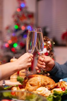 Closeup of couple clinking glass of wine during christmas dinner sitting at dining table in xmas decorated kitchen. Happy romantic family celebrating christmas holiday together enjoying winter season