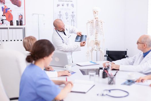 Expert doctor holding radiography during medical seminar for medical staff in conference room. Clinic therapist talking with colleagues about disease, medicine professional