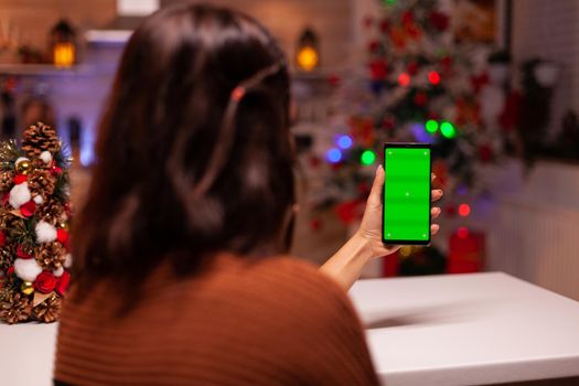 Festive person holding smartphone with green screen for modern technology on mockup template. Caucasian young woman watching digital device with chroma key to view background design