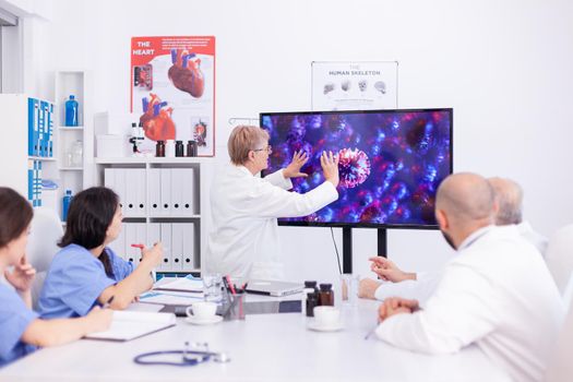 Hospital team discussing about coronavirus during meeting in conference room. Virolog specialist doctor discussing with colleagues about global pandemic because of dangerous virus, symptoms.