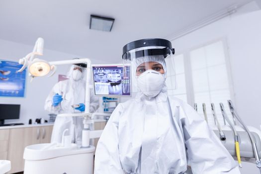 Patient point of view of dentist medical team treating teeth wearing precaution against covid in dental office. Stomatolog wearing safety gear against coronavirus during heatlhcare check of patient.