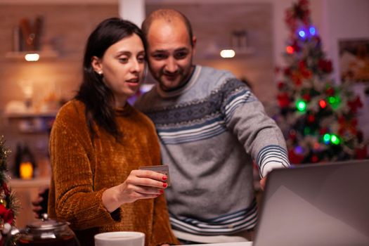 Happy family doing online shopping buying xmas present using credit card making transaction using laptop computer x-mas decorated kitchen. Cheerful family celebrating christmas holiday season together