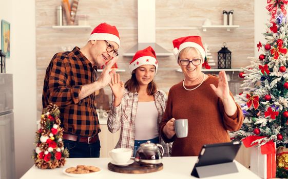 Senior parents and child celebrating christmas and talking with family during online call . Happy multi generation family wearing santa hat during video conference celebrating winter holidays, decorated kitchen.