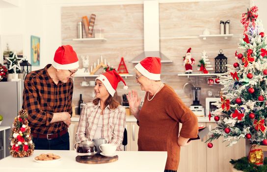 Senior man celebrating christmas with happy niece giving her gift box wearing santa hat. Happy loving grandparents celebrating winter holidays and relationship with granddaughter in home with x-mas decoration.