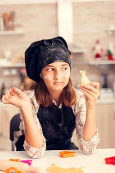 Grandchild on christmas day looking at shaped pastery wearing apron and bonette. Happy cheerful joyfull teenage girl helping senior woman preparing sweet cookies to celebrate winter holidays.