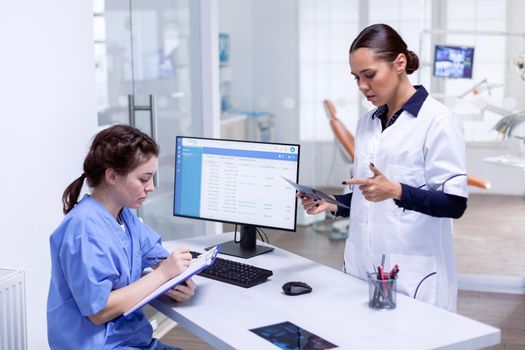 Dentist telling nurse patient teeth diagnosis holding x-ray in dental clinic. Stomatology assistant and teeth doctor discussing in reception of dental office