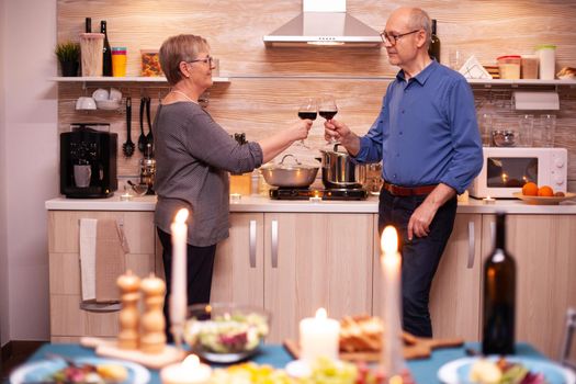 Senior couple celebrating anniversary with red wine in dining room. Aged couple in love talking having pleasant conversation during healthy meal.