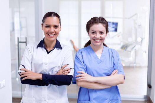 Cheerful dentistiry personal in teeth healtchare clinic smiling. Portrait of stomatology team in dental reception with arms crossed looking at camera wearing uniform.