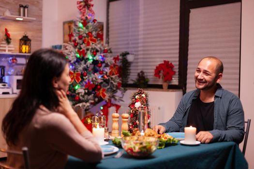 Happy family sitting at romantic dining table in xmas decorated kitchen enjoying christmas dinner together. Cheerful people enjoying winter holiday season celebrating christmastime