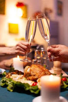 Closeup of couple clinking glass of wine during christmas dinner sitting at dining table in xmas decorated kitchen. Happy romantic family celebrating christmas holiday together enjoying winter season