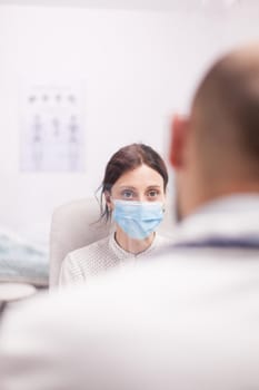 Young woman wearing protection mask against coronavirus during doctor examination in hospital office.